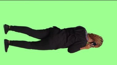 Dikey video: Afrikalı Amerikalı kadın yeşil ekran arkaplanı üzerinden konuşuyor, akıllı telefon hattı kullanıyor ve tüm vücudu izole edilmiş arka planda duruyor. Yetişkinlerin cep telefonlarını stüdyoda tutması.