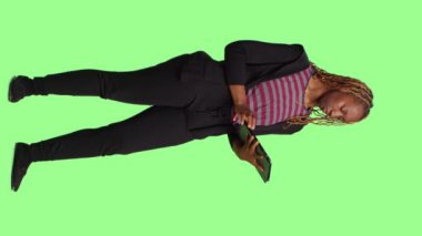 Dikey video: Yeşil ekranda dijital tablet kullanan modern kişi, tüm gövde yeşil ekran arkaplan. Dokunmatik ekranlı kablosuz taşınabilir aygıt, sosyal medya uygulaması üzerinde Browisng İnternet.