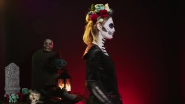 Santa Muerte mankeni stüdyoda gülüyor ve ürkütücü davranıyor. Ölü bayram günündeki La Cavalera Catrina gibi görünüyor. Gülümseyen ve çiçekli cadılar bayramı kostümü giyen bir kadın..