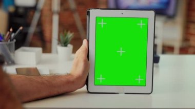 Ofis çalışanı elinde yeşil ekran şablonu gösteren dijital bir cihaz tutuyor, izole edilmiş model görüntüsünü krom anahtarla analiz ediyor. Kablosuz tablet ve boş telif alanıyla çalışmak. Kapat..