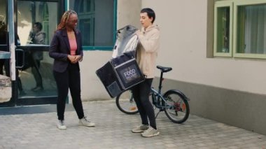 Po terminalindeki yemek paketini ödemek için kredi kartı kullanan bir kadın. Temassız ödeme, yemek siparişi. Sırt çantalı fast food restoranı kuryesi kadınlara yemek dağıtıyor..