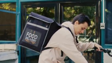Girişteki müşteriye fast food siparişi vermek için sırt çantası taşıyan, iş yerinde bisiklete binen kadın teslimatçı. Kadın kurye, erkek müşteriye paket servis yapıyor..