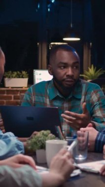 Dikey video: Çeşitli iş arkadaşları beyin fırtınası yapıyor, Afrikalı Amerikalı çalışanlar dizüstü bilgisayarlarında veri tabloları gösteriyor. İş toplantısında strateji planlayan insanlar, sunum tartışması, takım