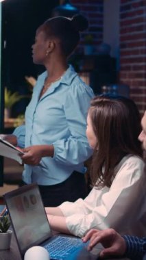 Dikey video: Çalışan iş görüşmesi sunumunda konuşuyor, rapor panosunu tutuyor. Çeşitli takımlar gelir istatistiklerini tartışıyor, satış stratejisini planlıyor, dijital tablolarda grafiklere bakıyor