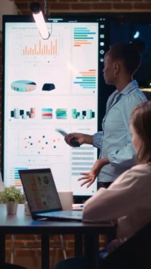 Dikey video: Çeşitli iş arkadaşları analitik rapor sunuyor, veri görselleştirmesine işaret ediyor, iş toplantısında kurumsal sunum yapıyor. Strateji tartışması, şirket araştırma istatistikleri