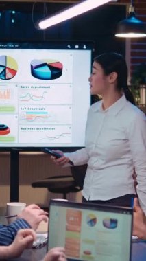 Dikey video: Şirket gelirleri istatistik sunumu üzerinde çalışan ekip iş toplantısında sunum yapıyor, mali strateji planlıyor. Analiz konularını tartışan iş arkadaşları toplantı odasında şema ve çizelge raporları hazırlıyorlar.