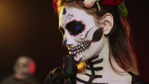 スタジオの背景には 死の衣装と花の花輪を身に着けている華やかな女神が聖サンタのマエルテのように振る舞っています 頭蓋骨のボディアートで死んだラ カヴァレラ カトリーナの女性 メキシコ文化 手持ち撮影 — ストック動画