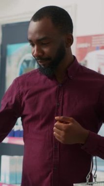 Dikey video: Afro-Amerikan müşteri eczane raflarındaki vitamin kutularına bakıyor, hap paketi broşürlerini okuyor. Delikanlı kasadan almak için takviye ve uyuşturucuları kontrol ediyor. El bilgisayarı