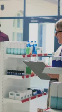 Dikey video: Afro-Amerikalı bir müşterinin eczacıya ilaç ve hastalık tedavisi için reçeteli kağıt vermesi. Mağaza raflarındaki takviye paketlerine bakan kişi. Üçayak atışı.