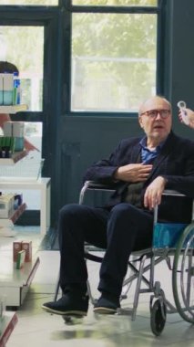 Dikey video: Tekerlekli sandalyedeki kişinin termometresini kullanarak, engelli bir adamın vücut ısısını ölçen sağlık uzmanı. Maluliyet dostu eczaneden reçeteli ilaç alan erkek hasta.