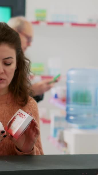 垂直视频 妇女向药剂师展示心脏科药物 询问有关购买治疗的医疗支持 人们在药店的收银机上看了一盒盒的补充剂和药品 — 图库视频影像