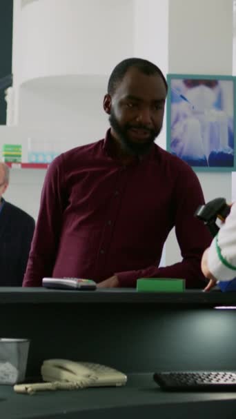 垂直ビデオ アフリカ系アメリカ人男性が携帯電話でNfc非接触支払いを使用しています 病気を治すために薬と薬の箱を購入するクライアント 薬局でのレジ — ストック動画