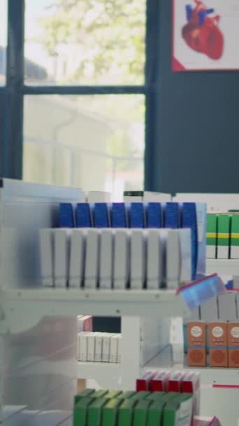 垂直ビデオ 若い男性の顧客は 病気の治療と薬の箱を見つけるためにアシスタントに処方紙を与える 薬局の棚のサプリメントパッケージを見ている人 — ストック動画