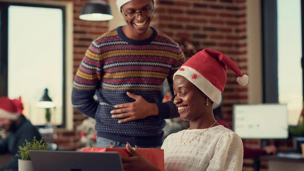 African american people exchanging xmas gifts in office decorated with christmas tree or ornaments. Man giving present to woman, celebrating winter holiday with festive decorations.