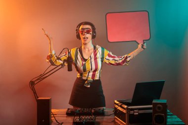 Bir kadın DJ konuşma baloncuğu tutuyor, izole bir kopya uzay kartonu üzerinde mesaj göstermek için, karton üzerinde reklam modeli şablonu. Stüdyoda reklam simgesi, tekno pikapları karıştırıyor.