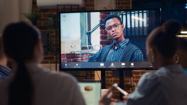 Afrika kökenli Amerikalı uzaktan kumandalı takım lideri video konferansında konuşuyor, ekranı kapatın, çeşitli insanlar gece vakti video konferansında konuşuyor. Ofis çalışanları iş yerinde telekonferansta sohbet ediyorlar.