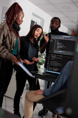 Masadaki programlama bilgisayarında html kodlama kodlaması yapan çok ırklı mühendis yazılım ajansındaki kaynak kodları ayrıştırıyor. Uygulama dili derleyen programcı çevrimiçi sunucu algoritmaları geliştiriyor.