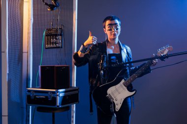 Kadın sanatçı stüdyoda baş parmak hareketi yapıyor ve heavy metal müzik eşliğinde canlı rock gösterisi yapıyor. Alternatif ses için gitar çalmak gibi olumlu bir hareket veya onay sembolü göstermek.