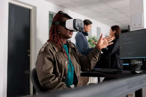 African american database admin working with virtual reality goggles to develop server app in it agency office, using source code. Checking programming language on cloud computing database, web