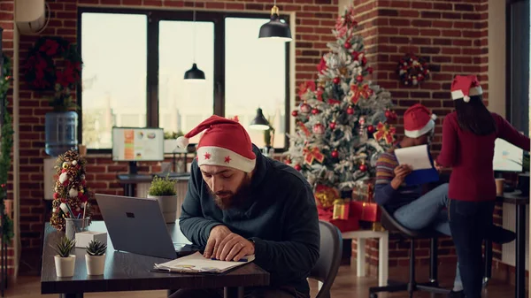 项目经理在有圣诞装饰品的节日办公室里用笔记本电脑工作 在寒假期间做启动报告工作 男人带着圣诞彩灯在太空发邮件 — 图库照片
