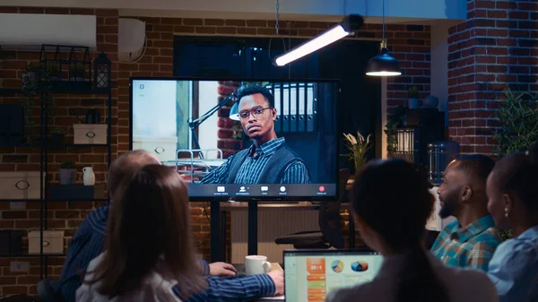 Remote team leader and employees company revenue presentation discussion in videocall, diverse people talking in videoconference at night time. Office workers chatting in teleconference