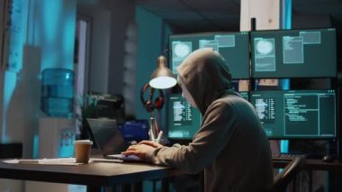 Maskeli bir veri hırsızı geceleri bilgisayar ağına sızıyor, bilgisayar üzerinde çalışıyor ve bilgi çalmak için birden fazla monitör kullanıyor. Gizli kimliği olan bir bilgisayar korsanı, sunucu güvenliği ihlali. El kamerasıyla..