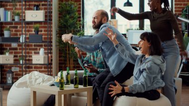 TV konsolunda video oyunları yarışması kazanan, oyun yarışmasını kutlayan, evinde mutlu hisseden çok ırklı insanlardan oluşan bir grup. Bira şişeleriyle oynayarak eğleniyorum..