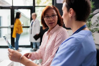 Doktor hemşire Asyalı hastayla radyografi taramasına bakıyor. Hastane bekleme alanında ortopedik tedaviyi açıklayan tıbbi asistan, tıp konsepti