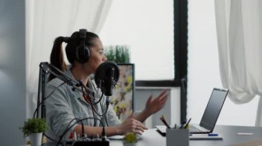 Dizüstü bilgisayarda konu listesini kontrol ederken mikrofondan konuşan internet radyo programı sunucusu. Popüler sosyal medya içeriği yaratıcısı modern stüdyoda otururken izleyicilere hitap ediyor.