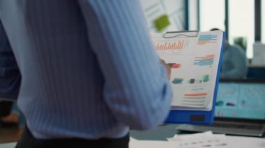Closeup of african american woman hands holding clipboard with financial data and sales charts in startup office. Focused employee analyzing performance indicators reading business statistics.