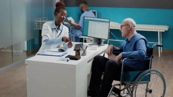 在轮椅上向病人展示X光扫描结果的女医生 在放射学上解释骨骼诊断 与身体残疾的老人交谈的专家 慢性功能障碍检查 — 图库视频影像