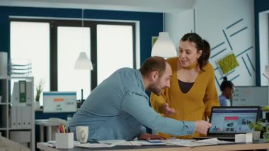 Smiling colleagues in startup office doing high five hand gesture celebrating business success standing at desk. Happy coworkers enjoying good results of team work looking at laptop with charts.