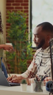 Dikey video: Ofis yöneticisi evde dizüstü bilgisayarla çalışıyor, dairede partneriyle oturuyor. Finansal rapor planlamak ve kurumsal e-posta göndermek için bilgisayarı kullanan bir adam, uzaktan masa başında çalışıyor. Üçayak