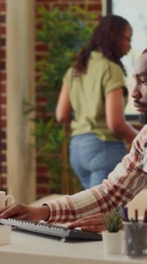 Dikey video: Profesyonel işçi bilgisayardaki online başlangıç verilerini analiz ediyor, kız arkadaşıyla evden çalışıyor. Genç adam muhasebe işi yapıyor, şirket bilgilerini ağdan kontrol ediyor..