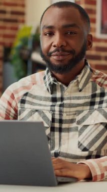 Dikey video: Evden uzakta çalışan Afro-Amerikan kişi, dizüstü bilgisayar kullanıyor ve satış ağında iş raporu yazıyor. Erkek serbest meslek öğrenimi dairede, muhasebe eğitiminde