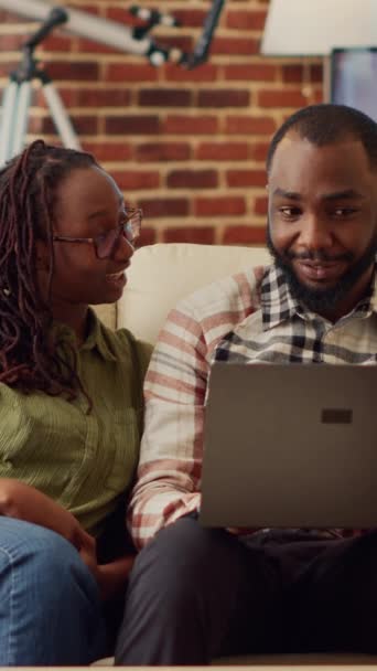 垂直视频 年轻夫妇一起在家里享受闲暇时光 坐在沙发上 在笔记本电脑上观看互联网视频 男人和女人笑着 玩在线社交 享受舒适的娱乐 — 图库视频影像