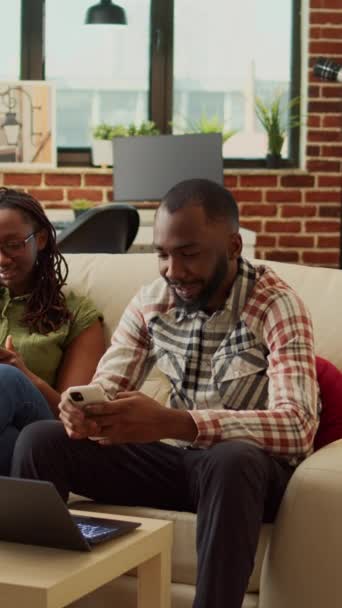垂直视频 快乐的人们舒适地坐在家里 在手机上浏览社交媒体应用程序 放松身心 男朋友和女朋友用智能手机舒服地睡在沙发上 — 图库视频影像