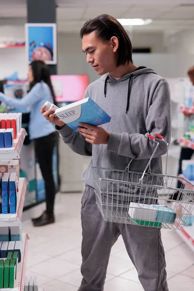 年轻人在药店里看着一盒安眠药 购买药物镇静剂来帮助医疗保健 阅读有关医疗 处方药的单张 — 图库照片