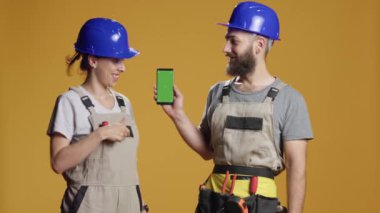 Stüdyoda inşaat işlerinde çalışan akıllı telefonları yeşil ekran ekranla gösteren müteahhitlerin portresi. Boş krom anahtar kopyalama alanı ile izole edilmiş model şablonu tutuluyor.