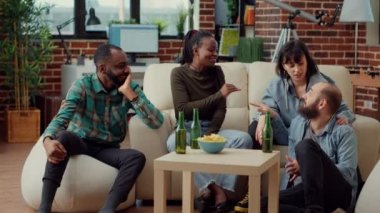 Bir grup arkadaş birlikte ev partisinde eğleniyor, hatıralardan ve arkadaşlıktan eğlence aktivitesi olarak bahsediyorlar. İnsanlar bira içip rahatlamak için gülüp eğleniyorlar. El kamerasıyla..