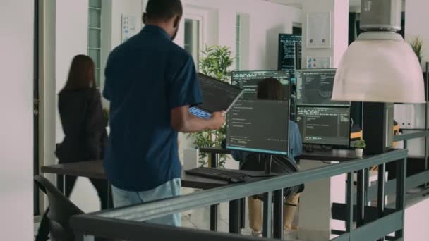 アフリカ系アメリカ人の開発者はノートパソコンを使ってコードを書き コンピュータにシステム情報を表示する ソフトウェア代理店のユーザーインターフェイスで動作するデータベースコーダー解析アルゴリズム — ストック動画