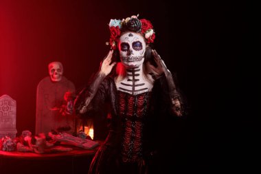 Ölüm tanrıçası kulaklıkla müzik dinliyor, kafatası makyajı yapıyor ve stüdyoda Santa Muerte kostümü giyiyor. Sesli kulaklıkla şarkı dinleyen ürkünç kadın, ölüyü kutluyor..