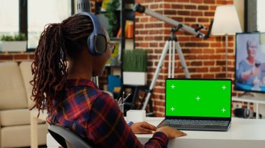 Kulaklık takan ve yeşil ekran ekranlı dizüstü bilgisayar kullanan kadın yönetici boş kopya alanı şablonuna bakıyor. İzole edilmiş renk tuşu ile çalışan girişimci arkaplan oluşturur.