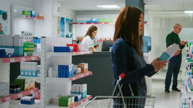 Eczane raflarındaki ilaç ürünlerine bakan çok ırklı bir grup müşteri, vitamin veya hap içeren ilaç ve kutuları kontrol ediyorlar. Takviye arayan müşteriler.