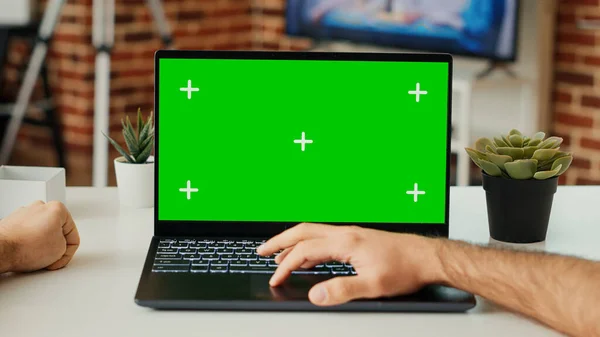 デスクで緑色のスクリーンテンプレートを使用してノートパソコンで作業している若い成人は 空白のクロマキーとポータブルコンピュータ上の隔離されたディスプレイを確認します コピースペースをモックアップしたPcを見てください 三脚が撃たれた 閉じろ — ストック写真