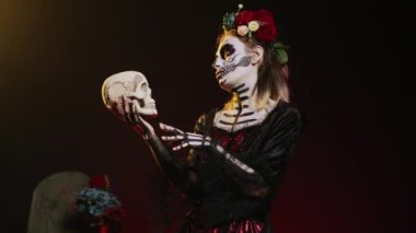 Kutsal ölüm tanrıçası stüdyoda kafatasıyla konuşuyor, Meksika cadılar bayramı geleneğini kutlamak için korkutucu ve dehşet verici davranıyor. Korkunç bir festival kostümü içinde vücut sanatıyla Noel Baba Muerte. El kamerasıyla..