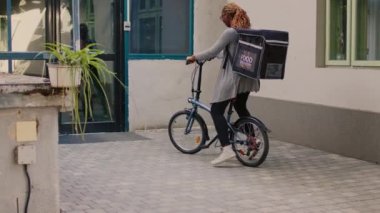 Ekspres yemek servisi kuryesi. Öğlen yemeğini kese kağıdında getiriyor. Ön kapıya fast food siparişi veriyor. Gülümseyen müşteri restoranı dışarıdan alıyor, paketli kadın bisikletli..