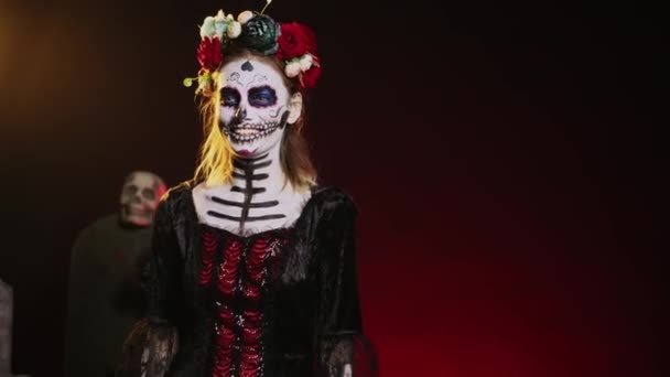 死んだ伝統的な休日の日にラ カヴァレラ カトリーナのように見える スタジオで笑って怖い演技神聖なメキシコのエンティティ 笑顔と花とハロウィンの衣装を着て 手持ち撮影 — ストック動画