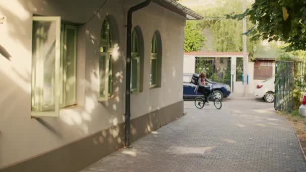 微笑的女人作为外卖信使和使用自行车 交付快餐餐诗意在前门 员工在阳光明媚的日子骑自行车为顾客提供餐馆食品 — 图库视频影像