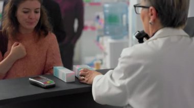 Kadın müşteri hapların parasını Ukalalık ve NFC ile ödüyor. Posta terminalinde ücretsiz ödeme yapıyor. Eczane masasından ilaç ve malzeme alan bir kadın, yazar kasadan. El kamerasıyla..